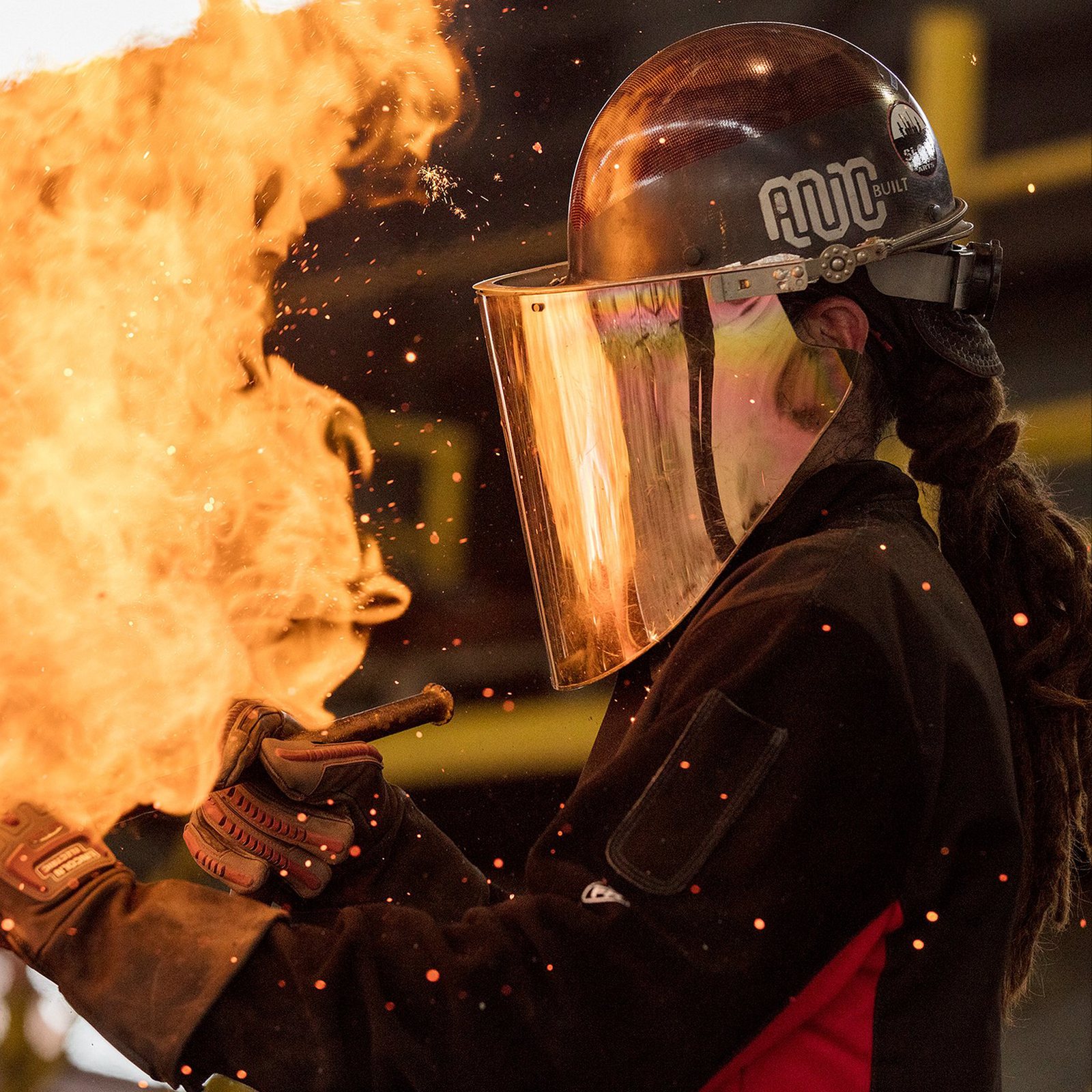 A trades worker in a face shield and ARC-branded hard hat, sparks flying